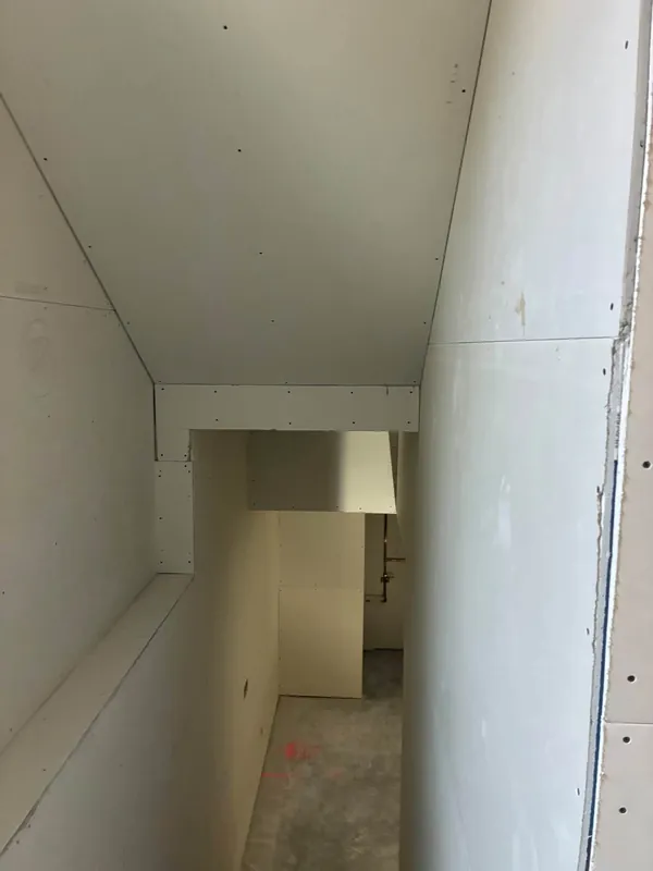 A stairwell ceiling and hallway boarded in new drywall, with the stair opening framed and the screws set